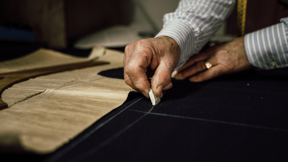Master tailor hand-cutting fabric with chalk markings